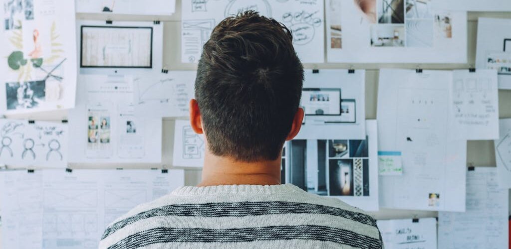 Man Wearing Black and White Stripe Shirt Looking at White Printer Papers on the Wall