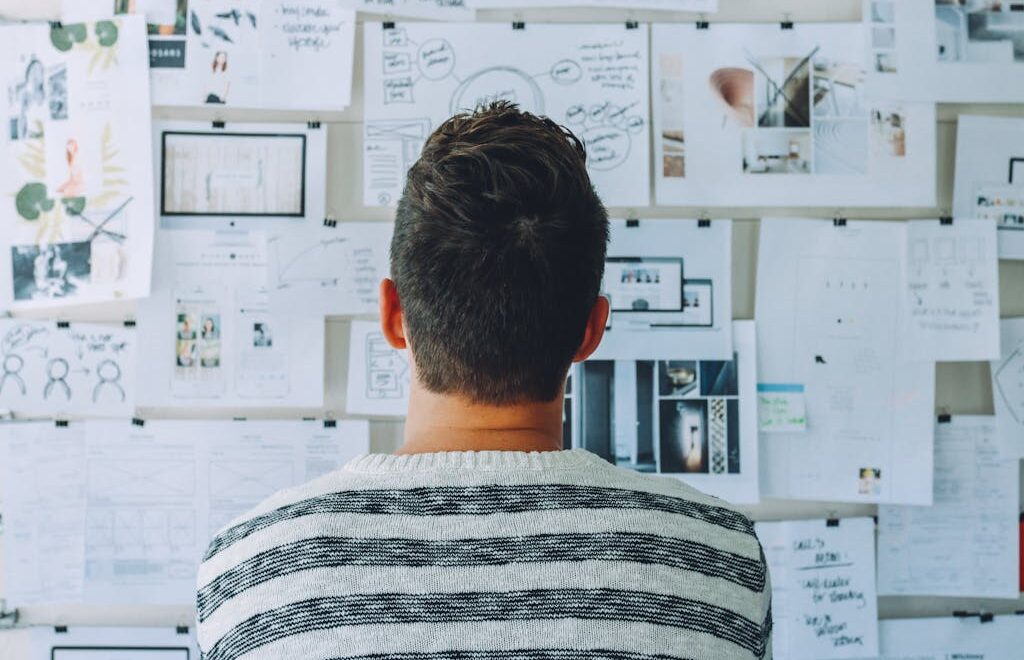 Man Wearing Black and White Stripe Shirt Looking at White Printer Papers on the Wall