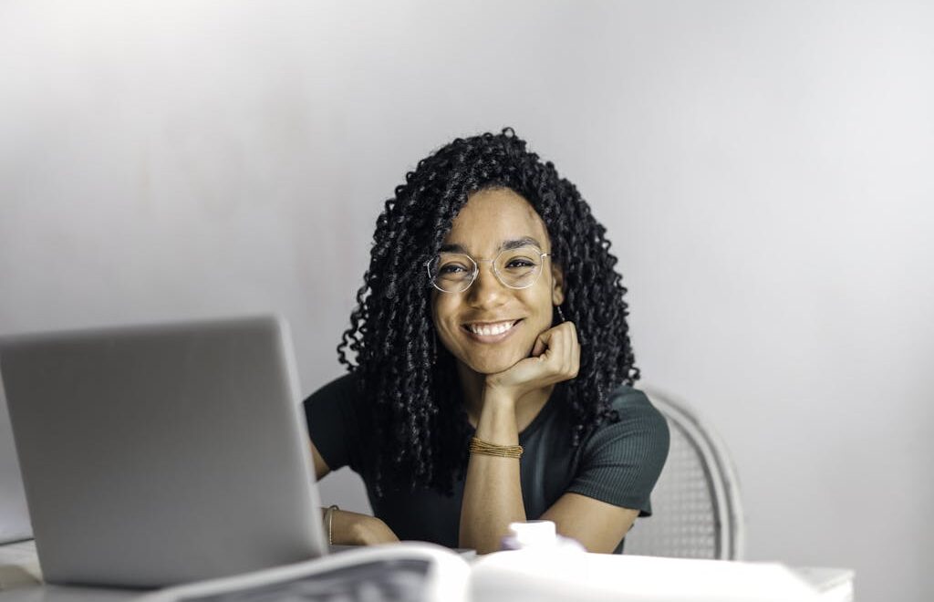 Happy ethnic woman sitting at table with laptop