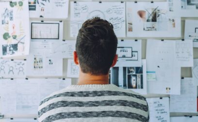 Man Wearing Black and White Stripe Shirt Looking at White Printer Papers on the Wall